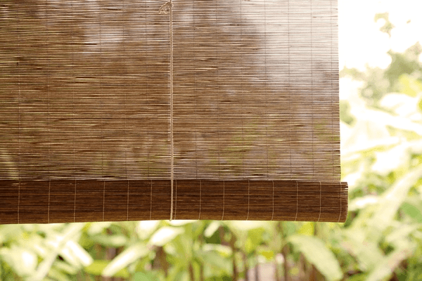 Natural recycled bamboo blinds hanging over a window with green garden views outside.