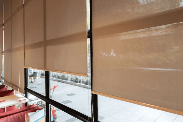 Motorized recycled blinds in a Dubai café or dining space, partially rolled down on tall glass windows with a view outside.