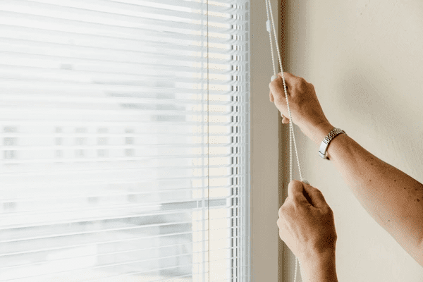 Close-up of hands adjusting the cord on horizontal white blinds in a modern Dubai home.