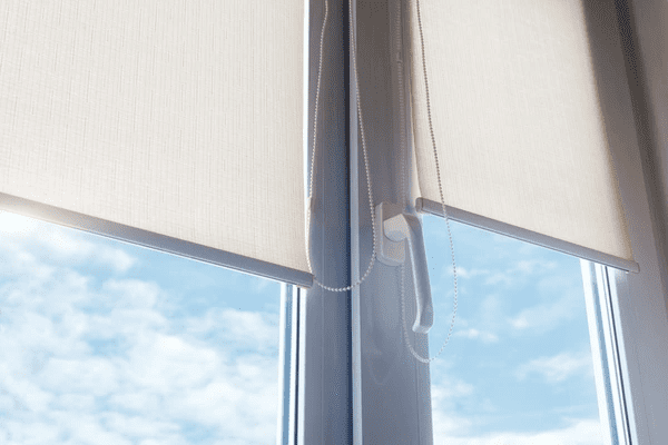 Modern roller blinds partially rolled down on a window with clear blue sky visible outside.