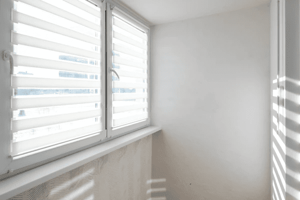Modern white zebra blinds partially drawn on two side-by-side windows in a minimalistic, sunlit interior with a soft white color scheme.