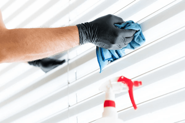 Gloved hands cleaning sleek white window blinds with a blue cloth and cleaning spray, showcasing top hygiene and care trends in Dubai.