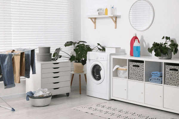 Stylish laundry room in Dubai with sleek white blinds, washing machine, modern storage, indoor plants, and drying clothes.