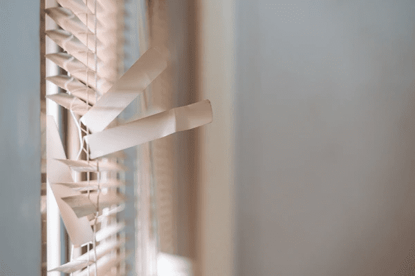 Close-up of damaged white window blinds with broken and bent slats in a cozy home interior.