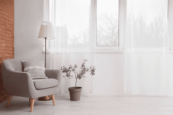 Cozy corner with sheer anti-condensation blinds in a modern Dubai home, featuring a soft grey armchair and warm lighting.