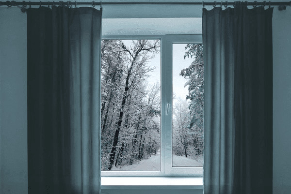 Thermal anti-condensation curtains in a cozy Dubai room, framing a snowy winter landscape outside a double-glazed window.