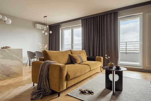 Contemporary living room with mustard sofa, large windows, and dark velvet anti-condensation curtains enhancing warmth and style.