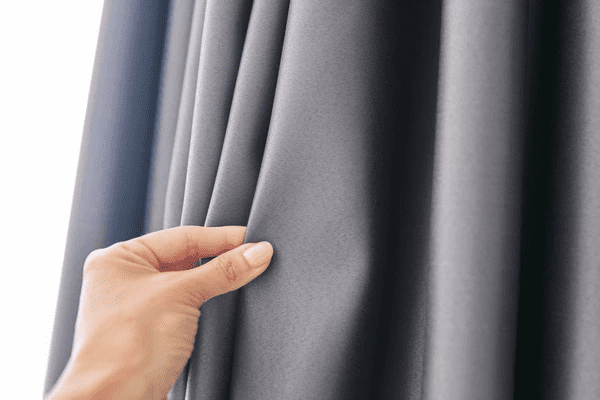 Close-up of a hand touching elegant gray blackout curtains, showcasing premium fabric and sleek folds for Dubai interiors.