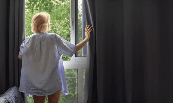 Woman opening sleek blackout curtains in a cozy Dubai home filled with morning light and lush green views.