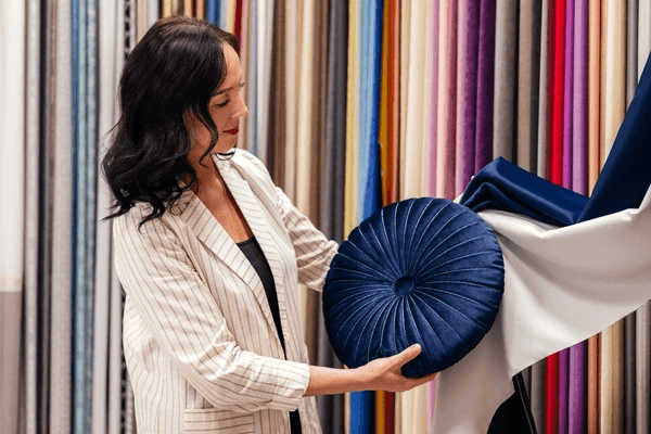 A woman selecting luxurious fabric and a velvet cushion at Emirati Blinds & Curtains, the best curtains store in Dubai 2025.