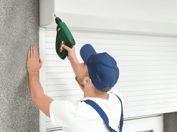 Professional installer using a power drill to fit modern white roller shutters on a home in Dubai 2025.
