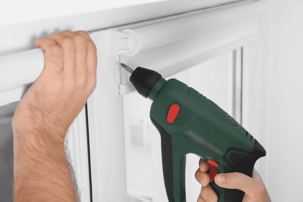 Close-up of a person using a drill to install white roller blinds on a modern window frame in Dubai 2025.