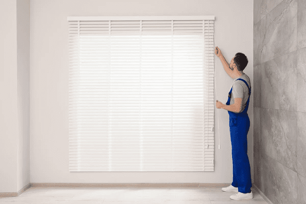 Worker in blue uniform operating newly installed white horizontal blinds in a modern interior space in Dubai 2025.