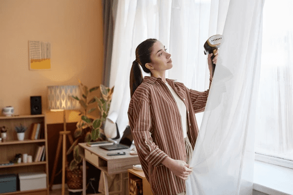 A woman adjusting easy-to-maintain sheer curtains in a cozy, stylish living room, ideal for modern Dubai homes in 2025.