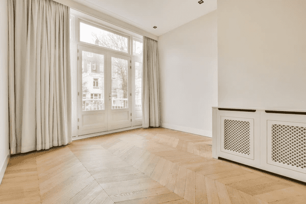 Bright empty living room with sleek beige noise reducing curtains covering a large window and door in a modern Dubai home.