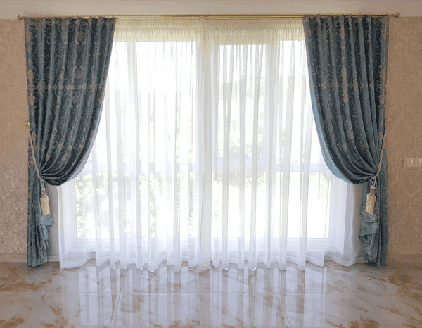 Classic living room with luxurious blue velvet curtains and sheer white drapes over a large window.