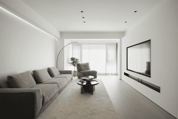 Elegant minimalist living room with soft white quality curtains, large grey sectional, and built-in flat-screen TV.