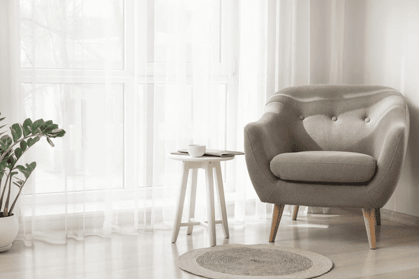 Modern cozy living room with sleek gray armchair, sheer white curtains, round rug, and indoor plant – showcasing top-rated sheer curtain trends for Dubai homes in 2025