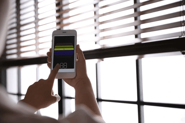 A woman controls sleek wooden blinds using a smartphone app, demonstrating smart and advanced home & furniture blinds technology in Dubai 2025.