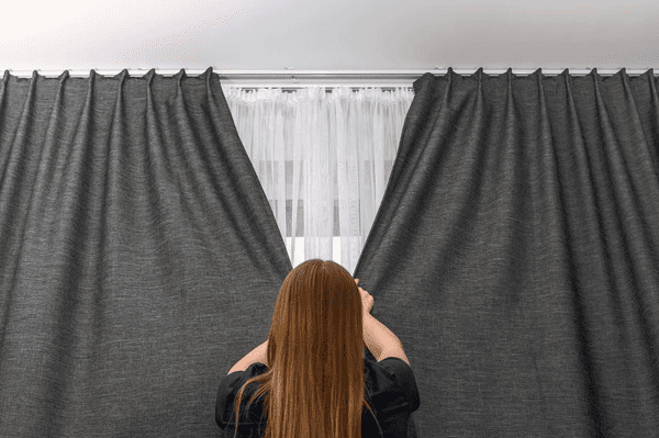 Young woman closing luxurious gray blackout curtains in a bright, contemporary Dubai room.