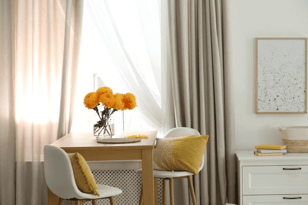 Beige and white curtains behind a minimalist dining setup with yellow floral decor in a Dubai home