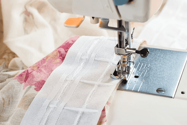 Detailed process of creating luxurious, modern curtains. A sewing machine is used to attach curtain tape to elegant floral fabric, a key step in producing high-quality, trendy curtains. These are perfect for any cozy, sophisticated home in Dubai.