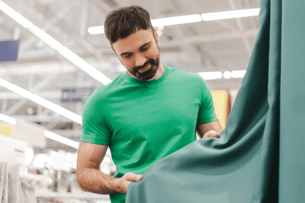 Smiling man in green shirt examining premium curtain fabric at a store, symbolizing selection of top-rated curtains in Dubai 2025.