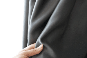 Close-up of a hand gently touching thick gray blackout curtain fabric, showcasing its softness and quality finish.

