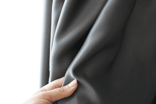 Close-up of a woman's hand gently touching high-quality grey blackout curtain fabric in a well-lit room.