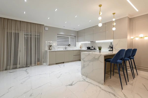 Luxury modern kitchen in Dubai with white marble finishes, gold lighting, and sheer floor-length curtains.