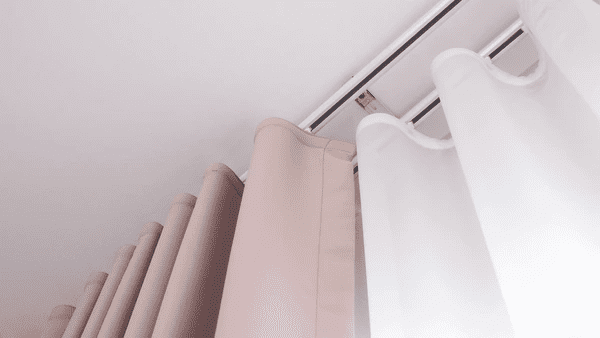 Close-up of dual-layered pink and white curtains hanging from a sleek ceiling-mounted track system in a contemporary interior.