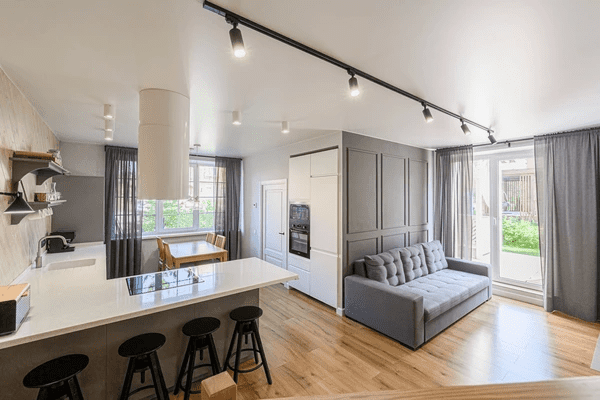 Modern open-concept living and kitchen space with grey track curtains framing large windows and sliding doors.