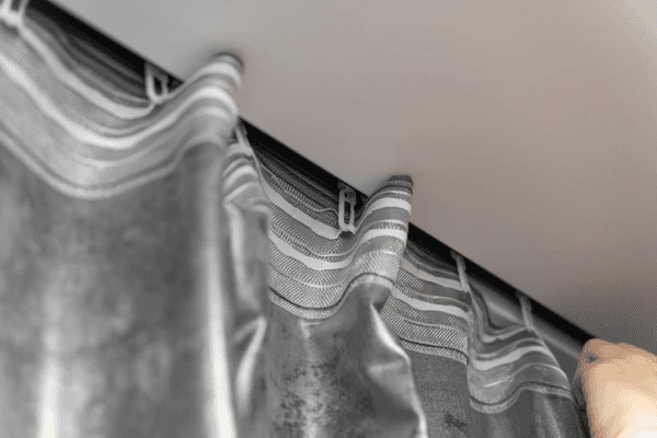 A hand adjusting sleek grey track curtains mounted on a ceiling rail inside a modern Dubai home.

