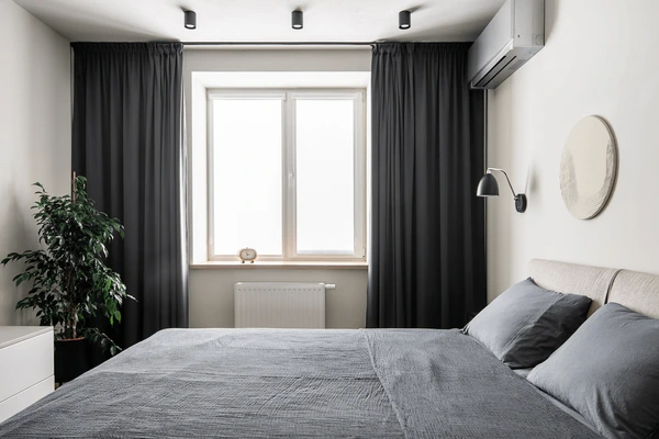 Minimalist Dubai bedroom with soft grey bedding, white walls, and full-length black blackout curtains enhancing coziness and privacy.

