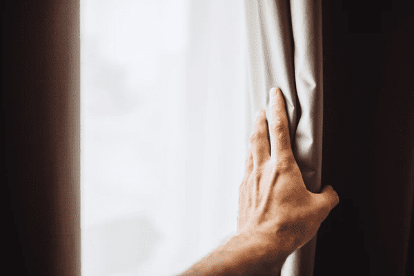 Close-up of a hand gently touching thick blackout curtains drawn beside a bright window, emphasizing luxury and coziness in a Dubai home.

