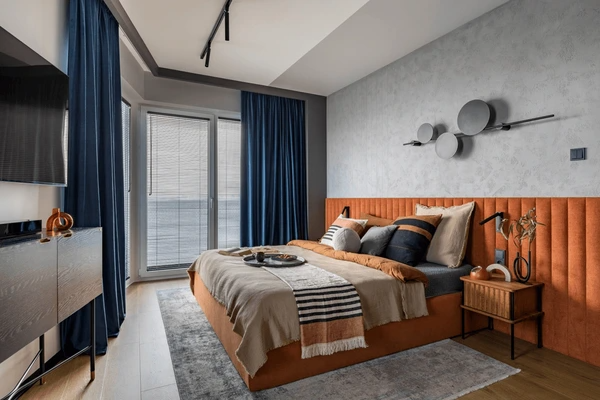Luxurious blue bedroom curtains in a stylish modern Dubai apartment with orange headboard and wooden accents.
