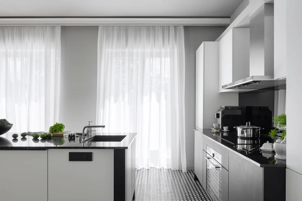 Bright white kitchen in Dubai with sheer white curtains, black countertops, and modern monochrome design.

