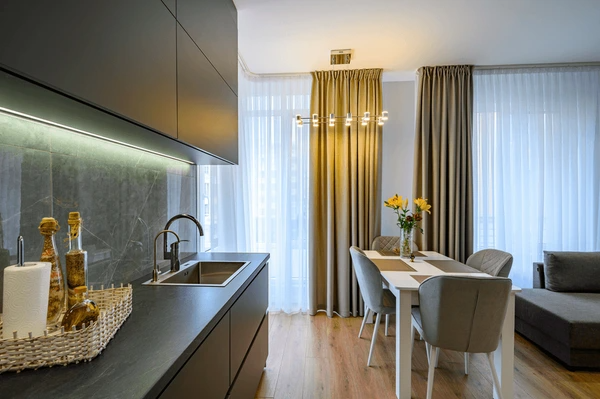 Contemporary Dubai kitchen with sleek black cabinetry, a dining table, and floor-to-ceiling beige kitchen curtains over large windows.