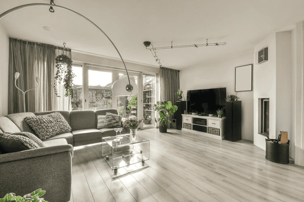 Modern living room in Dubai with floor-to-ceiling track curtains, grey sectional sofa, glass coffee table, and indoor plants.

