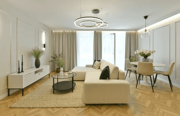 Contemporary living room with soft beige curtains, modern lighting fixtures, a cozy L-shaped sofa, and a minimal round dining table in Dubai 2025.