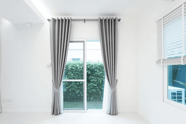 Modern white room in Dubai with neatly tied grey blackout curtains on a glass door, blending privacy with a clean and elegant minimalist aesthetic.

