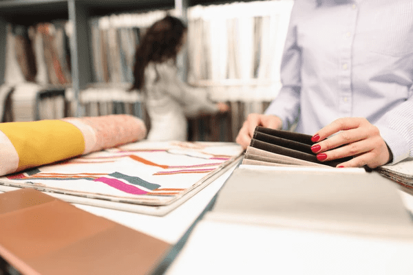 A close-up of a woman selecting high-quality fabric for soundproof and acoustic curtains in a fabric store. The fabric choices are displayed in neat stacks, with vibrant patterns and elegant textures.

