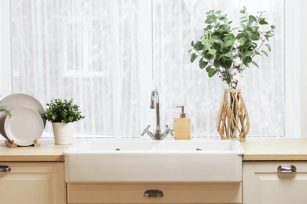 Fire-resistant lace curtains installed above a bright kitchen sink with plants and natural light.