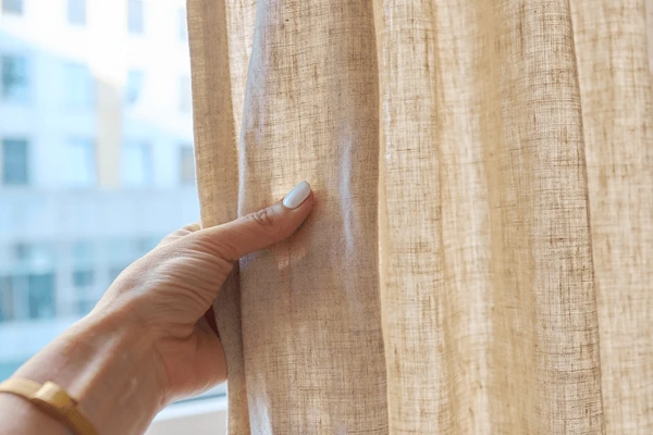 Hand touching beige linen curtain fabric, highlighting its natural texture and soft finish for stylish Dubai homes.