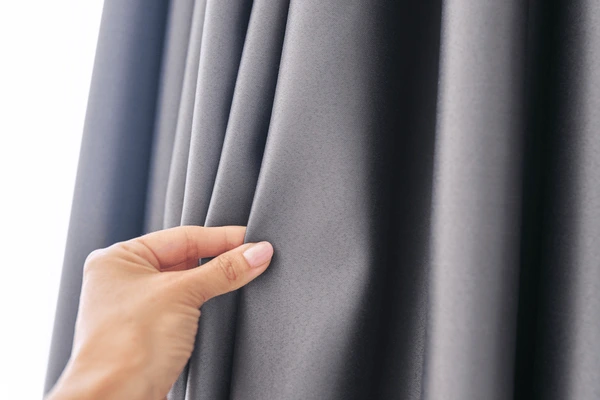 Hand touching thick gray blackout curtain fabric, showing smooth texture and premium quality for Dubai homes.
