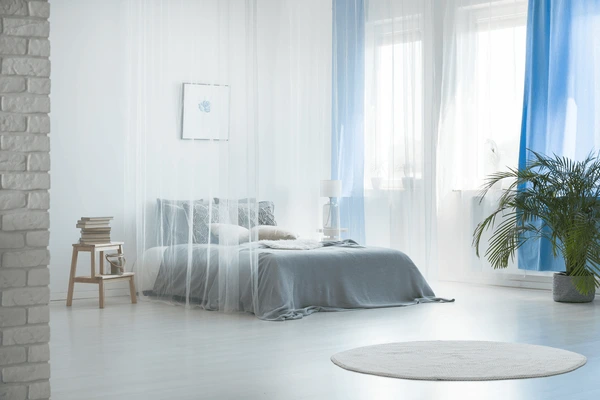 Bright bedroom with sheer white curtains layered over blue drapes, minimalist décor, and natural light in a Dubai home.