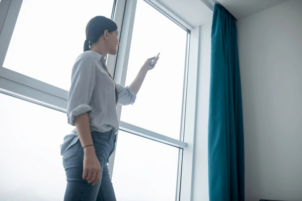 Woman using a remote control to operate modern blue curtains in a bright home interior, showcasing luxury and smart living trends in Dubai 2025.
