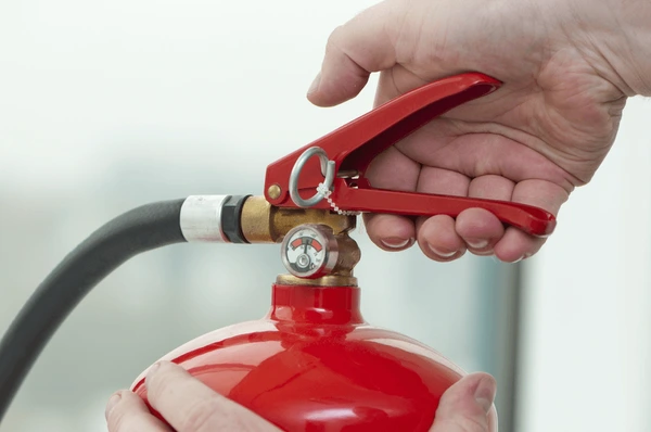 Close-up of a person’s hand pressing the trigger of a fire extinguisher, demonstrating fire safety precautions in Dubai 2025.
