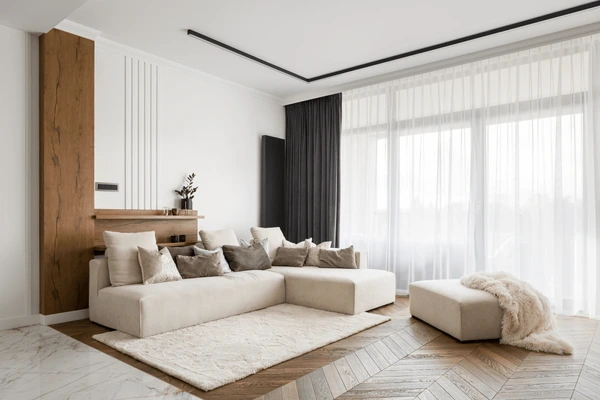 Stylish Dubai living room with floor-to-ceiling sheer white curtains paired with dark blackout drapes, a beige sectional sofa, and cozy décor.