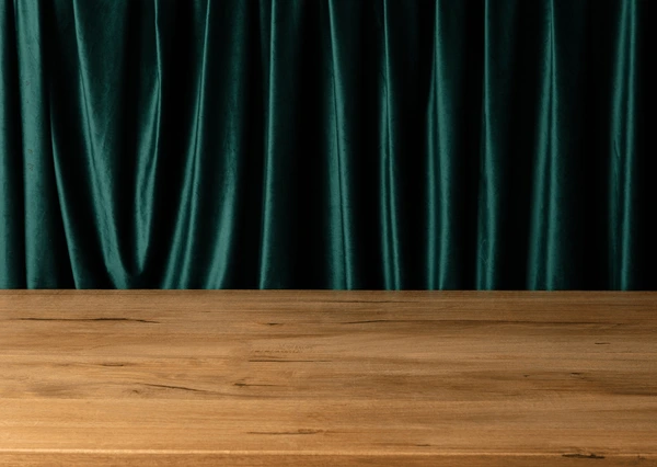 Elegant emerald green velvet curtains behind a polished wooden surface, creating a rich and luxurious interior look.

